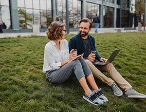 Deux salariés assis sur l'herbe devant la façade de leur entreprise